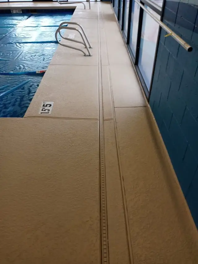 Cool deck coating on a covered deck beside a lap pool, depth markings visible on the surround