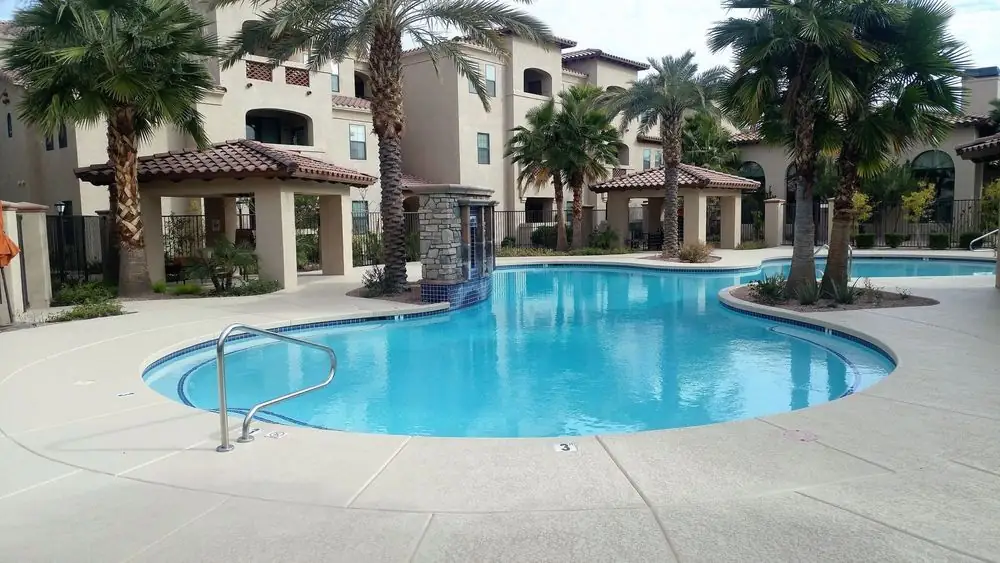 A finished cool deck surround at a Valley condominium, palms and stone pillars beyond it