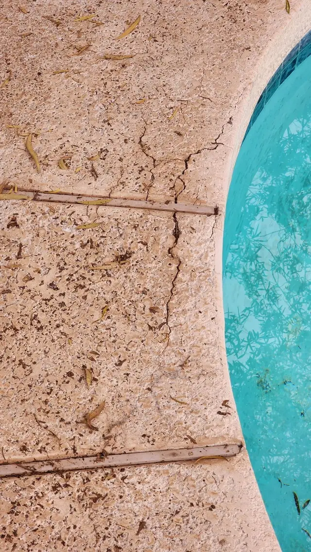 A worn pool deck with cracked coping, photographed before resurfacing